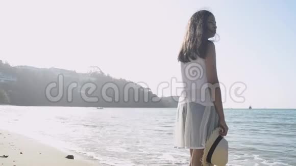 亚洲可爱的女孩戴着草帽穿着休闲装站在阳光下的海滩上视频的预览图
