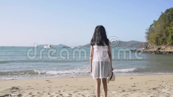 亚洲可爱的女孩戴着草帽穿着休闲装站在阳光下的海滩上视频的预览图