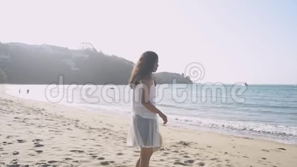 亚洲可爱的女孩拿着草帽在阳光下快乐地在海滩上旋转视频的预览图