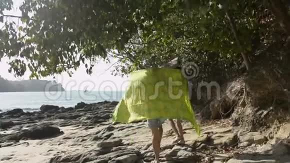 母亲和她的女儿在烈日下用一块大布走在一起一起在海岸上散步视频的预览图