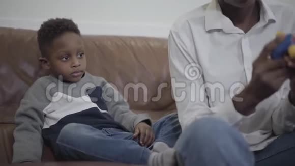 可爱的非裔美国女人和她可爱的小儿子坐在舒适的客厅里的沙发上玩玩具视频的预览图