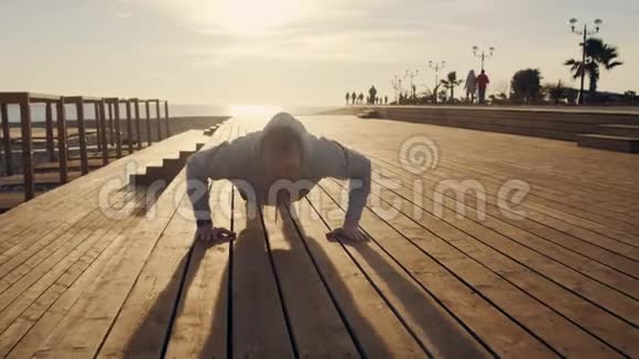 男运动员在阳光明媚的傍晚在海边的城市堤岸上做俯卧撑视频的预览图