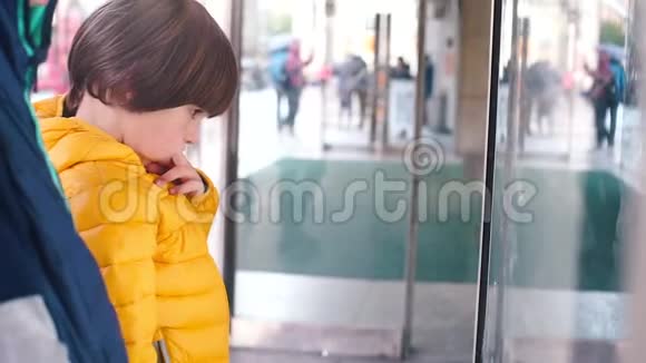 孩子站在城市的商店橱窗里吮吸手指视频的预览图