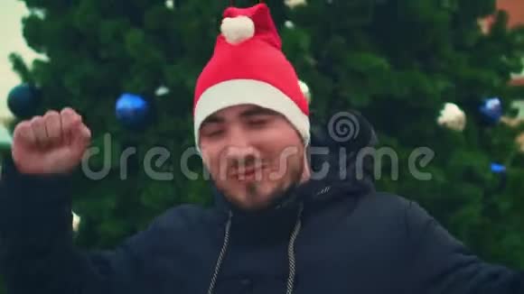 一个英俊的男人穿着圣诞帽西装在模糊的森林背景下跳舞的肖像视频的预览图