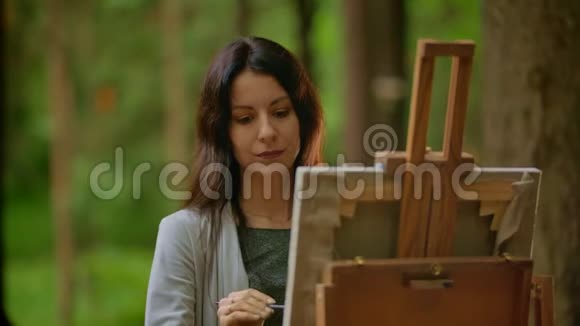 一个美丽的黑发女人在公园的画布上画一幅画的肖像视频的预览图