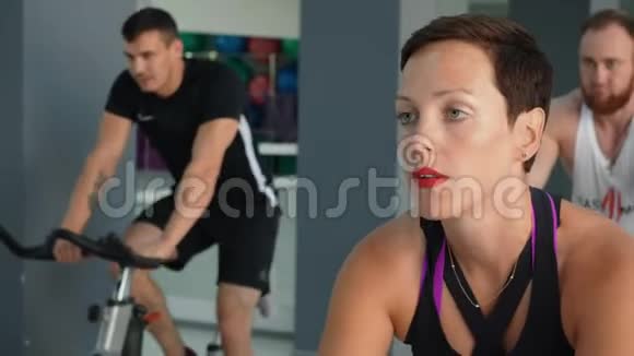 漂亮的女人在健身房的自行车课上训练肖像健身女子在室内自行车上训练自行车健身房体育运动视频的预览图