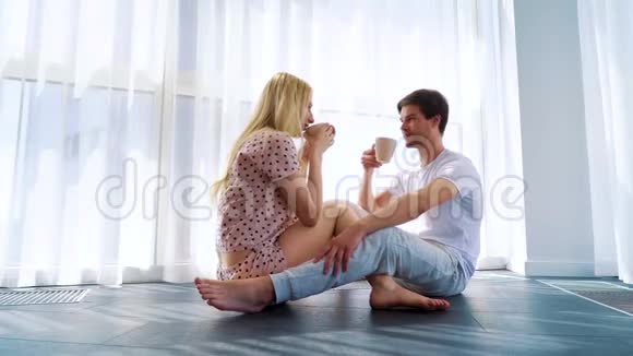 早晨幸福的情侣在阳光下坐在地板上喝咖啡视频的预览图