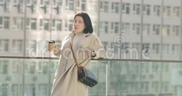 疲惫的白种人黑发女人打哈欠和喝咖啡的肖像成功的年轻女商人站在视频的预览图