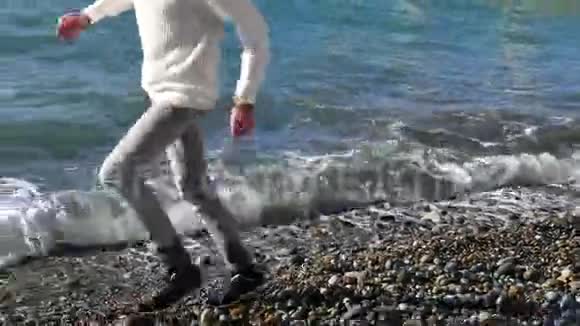 年轻人在岩石和海水上奔跑在鹅卵石海滩上慢动作视频的预览图