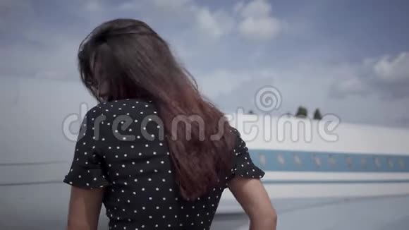 快乐的年轻黑发女孩摆着姿势看着白色大飞机前的摄像机头发在飞舞视频的预览图