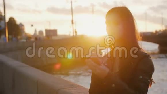 年轻漂亮的女孩在夕阳的明亮光线下在桥的背景上自拍4K视频的预览图