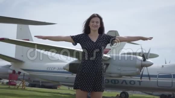 快乐的年轻黑发女孩穿着短裙子看着镜头两臂分开模仿飞机进入视频的预览图