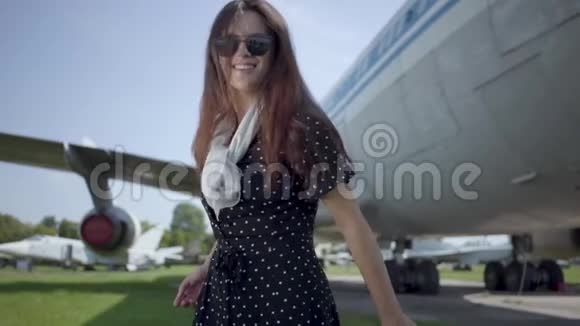快乐顽皮的黑发女孩戴着太阳镜在大飞机前旋转看着相机夏天快乐视频的预览图