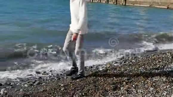 穿着毛衣牛仔裤和运动鞋的年轻人在沙滩上漫步视频的预览图