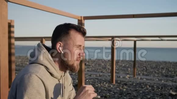 男人正在检查他的耳朵里的免提装置坐在海边视频的预览图