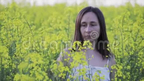 一个迷人的女人走过一片黄色的油菜地女孩安息在清新的空气中美丽的夏日风景视频的预览图