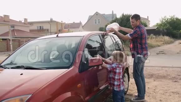年轻的父亲给红色的汽车浇水而小儿子则车窗缓慢地转动视频的预览图