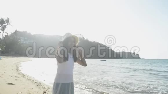 亚洲可爱的女孩戴着草帽和休闲服早上在阳光下站在海滩上放松视频的预览图