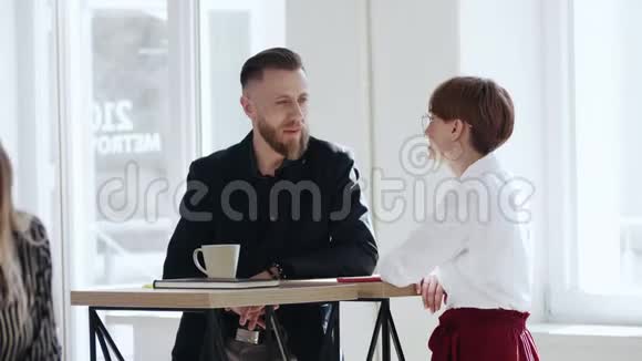 快乐的微笑胡须中年男性老板与年轻的同事女士交谈站在时尚的阁楼办公桌上视频的预览图