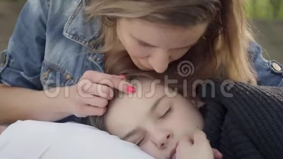 可爱的男孩睡在妈妈手里女人在公园里抚摸她孩子的头发户外休闲母性视频的预览图