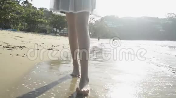 穿着休闲服装的亚洲女孩的腿在阳光下赤脚在海滩上行走具有波浪的低角度视图视频的预览图