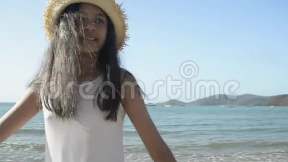 穿着休闲服装戴草帽的亚洲可爱女孩正在阳光下转身悠闲地在海滩上散步视频的预览图