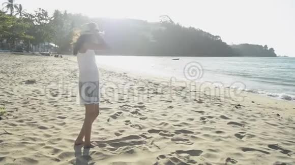 早上亚洲可爱的女孩戴着草帽和休闲服站在阳光下的海滩上视频的预览图