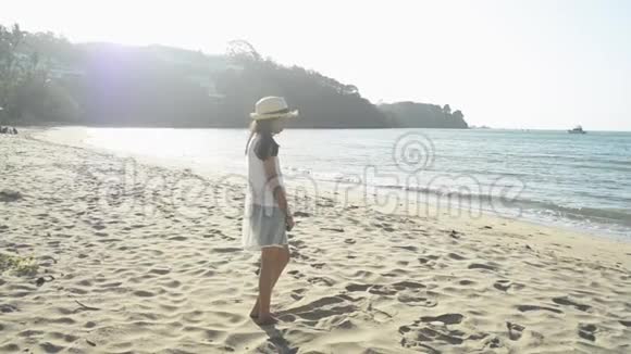 早上亚洲可爱的女孩戴着草帽和休闲服站在阳光下的海滩上视频的预览图