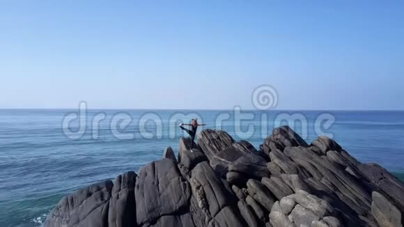 穿黑色运动服的女士站在蓝色海洋的瑜伽姿势上视频的预览图