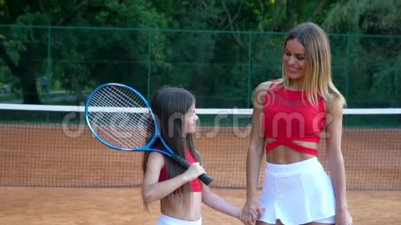 成人和小网球运动员牵手在网球场上社交母亲和女儿是女运动员视频的预览图