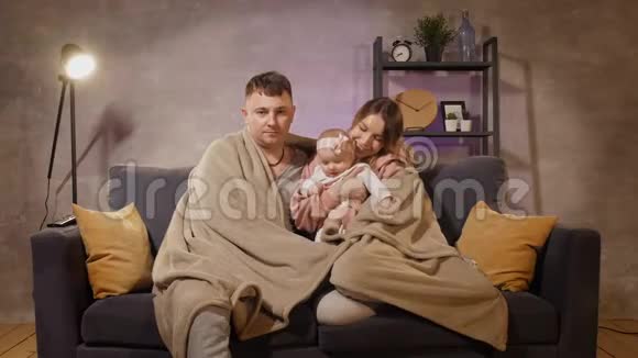 一个年轻的家庭坐在沙发上看电视妈妈爸爸和女儿都很开心视频的预览图