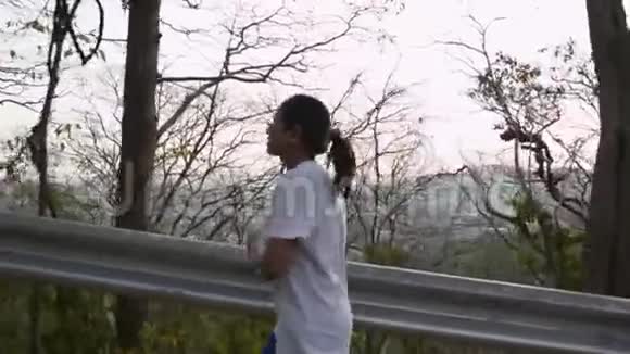 亚洲女人在路上穿过小山夏季一名女跑步者瞄准热带森林中的山视频的预览图