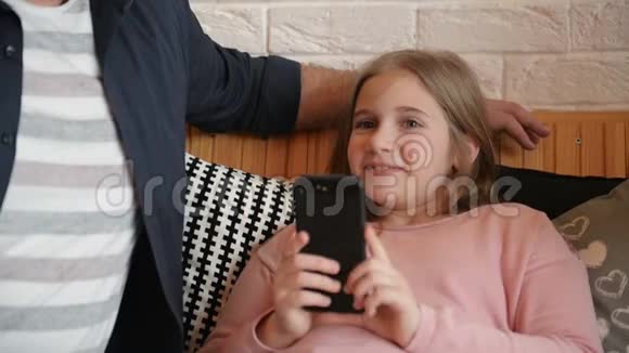 年轻的父亲和女儿一起在咖啡厅喝茶女孩拿着她的智能手机视频的预览图