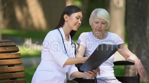 微笑护士给坐在公园轮椅上的老妇人做脊柱x光检查恢复正常视频的预览图