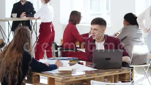 快乐微笑的男商务经理与坐在办公室桌上的年轻金发同事女士交谈健康的工作场所视频的预览图