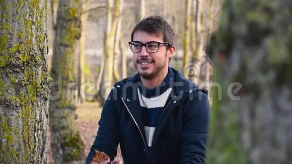 快乐的年轻人微笑着张开双臂在秋天的公园里扔树叶视频的预览图