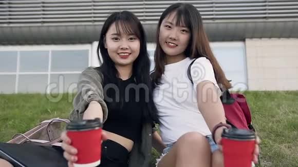 靠近迷人的微笑的亚洲女孩带着咖啡杯看着城市建筑附近的摄像机视频的预览图