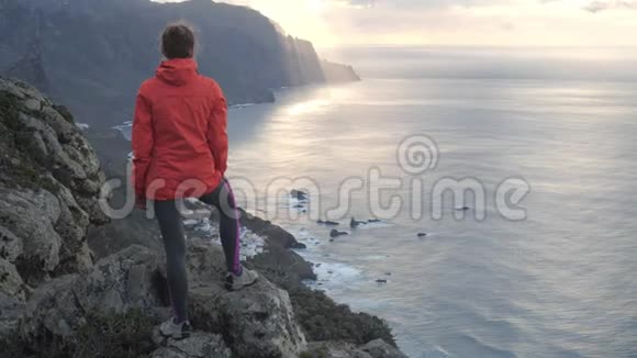 一位年轻女子站在山顶上靠近海洋上的悬崖边缘在特内里费岛上观察日落夫人在视频的预览图