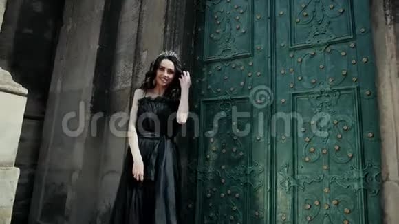 苗条的小姐黑发的穿着黑色衣服戴着皇冠摆着姿势靠近老建筑视频的预览图