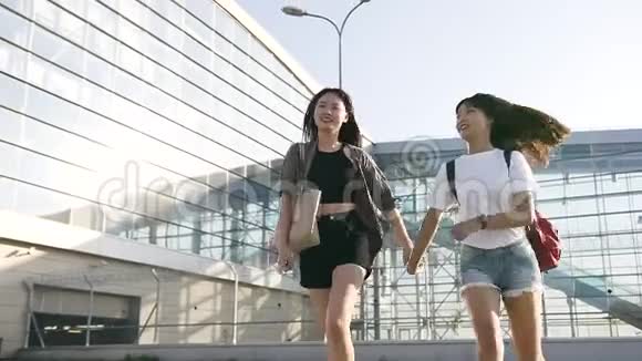 年轻漂亮的亚洲女孩穿着时髦的衣服手牵着手在现代时尚的附近奔跑视频的预览图