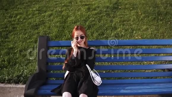 带着红发戴墨镜和黑色连衣裙的白种人微笑着在手机上休息时说话的画像视频的预览图
