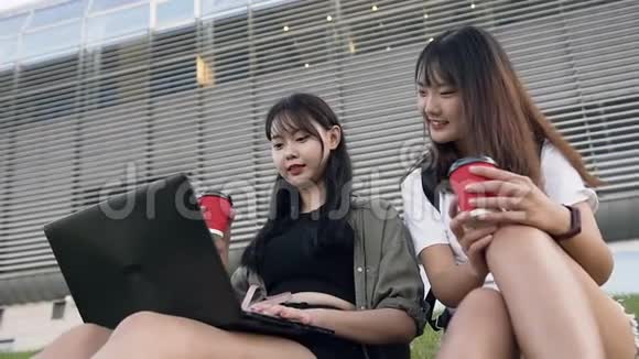 热情洋溢的亚洲年轻女性坐在草地上在现代电脑旁修改照片视频的预览图