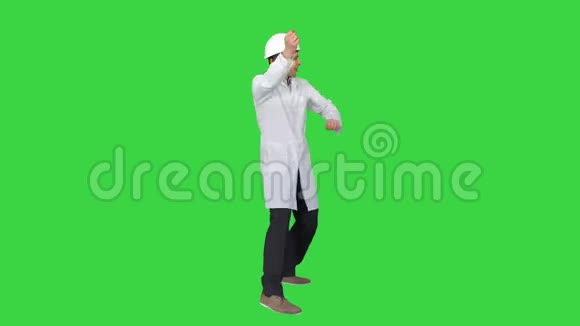 年轻的工人戴着白色长袍的头盔喜欢在绿色屏幕上跳舞Chroma键视频的预览图