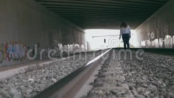 年轻女子走在充满涂鸦的隧道中的火车轨道之间慢动作视频的预览图