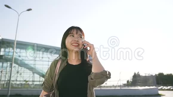 在机场大楼附近的移动电话上一位长相英俊的25岁亚裔黑发女郎在白天交谈视频的预览图