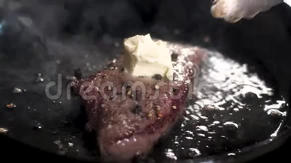 厨师铺黄油炸牛排油融化流到热锅里胡椒牛排是油煎的喷油和喷油视频的预览图