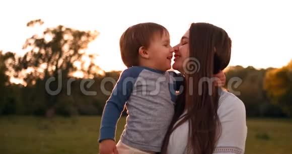 儿子亲吻母亲坐在夕阳下的田野里拥抱和慈爱的母亲妈妈今天视频的预览图