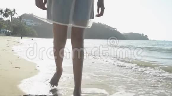 亚洲女孩戴着草帽穿着休闲服装赤脚在阳光下在海滩上散步低角度视角视频的预览图