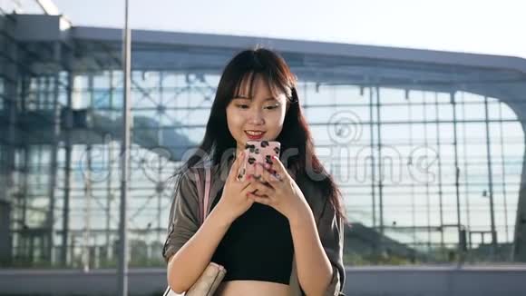 乔昆德25岁快乐的亚洲女士留着长发穿着时尚的衣服她的智能手机接近现代视频的预览图