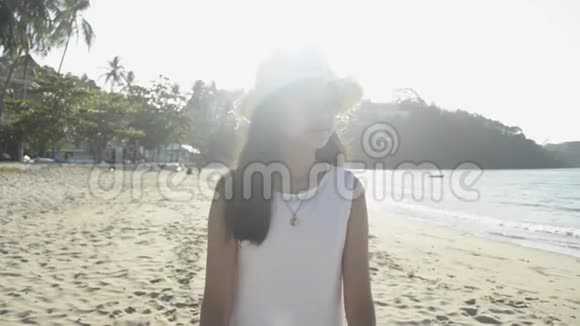 亚洲可爱的女孩戴着草帽和休闲服装在阳光下漫步在海滩上视频的预览图